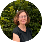 Porträtfoto von Patricia Threin. Sie trägt ein schwarzes Oberteil und steht vor einem Busch.